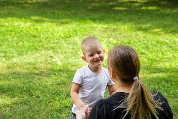 Mom and son holds hands in nature, park, outdoor. Laughing smiling child. Trust and love in family. Summer family walk