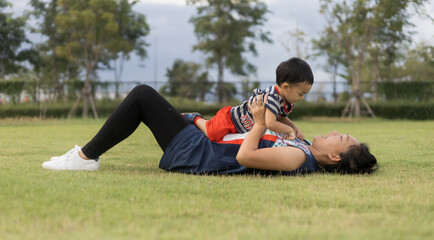 An Asian mother and toddler son (1-year-old) are playing, laugh, and relax together in the garden on a cloudy day.