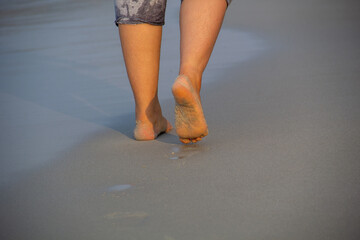 woman walking on sand beach leaving footprints in the sand.