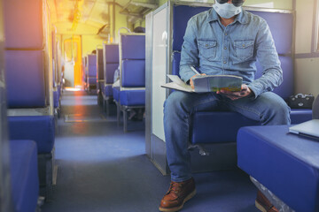 Hipster man with face mask sitting and traveling by train with map to finding destination in new normal style. New normal travel concept.