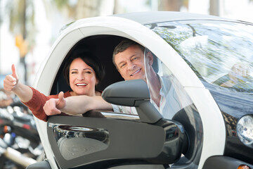 Portrait of smiling man and woman standing near twizy electric outdoors