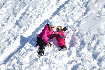 Fototapeta na wymiar Happy family mother and girl daughter playing and laughing in winter snow. Little girl and her mother playing outdoors at sunny winter day. Active winter holidays concept.