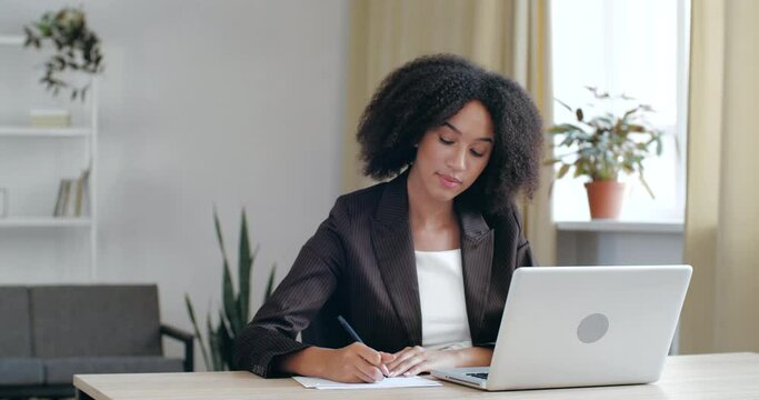 Focused millennial African professional financial advisor holding video call support services with customer. Motivated concentrated young American student studying on online courses, writing notes