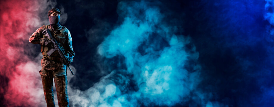 Special forces soldier of  standing in the smoke.  Infantryman fighting with terrorism. Commando on smoky red and blue light background with rifle.