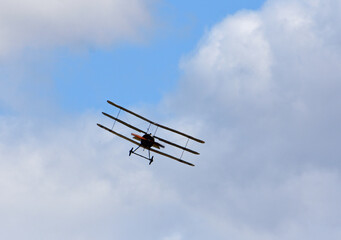 Vintage Sopwith Triplane in flight with clouds and blue sky.	