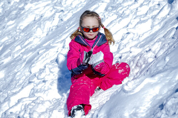 Fototapeta na wymiar Young Girl Sitting On The Snow Mountain and playing with snow ball .