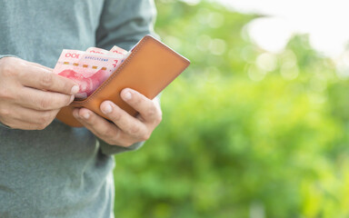 Man counting and checking Chinese banknote in his wallet. Outdoor shooting with green blur background