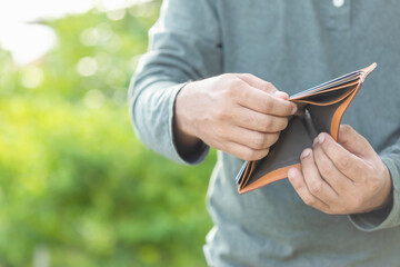 Man holding empty wallet. Money problem concept. Outdoor shooting with green blur background