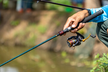 Fishing reel and rod in fisherman hand in a pond