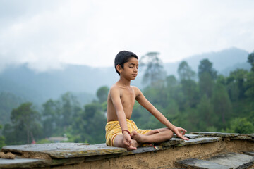 A young indian cute kid doing yoga in the mountains,wearing a dhoti