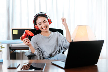 Funny Young woman wearing earphones playing computer game on laptop with joypad.