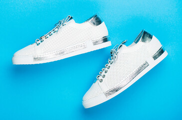 Overhead shot of running shoes. Close up, modern fashion shoes made of laces. Sneakers isolated on blue background, fashion. White shoes. Pair of white shoes on blue background