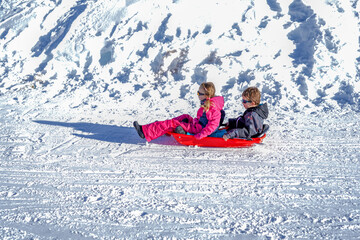 Fototapeta na wymiar Two joyful kids sledding down the hills on a winter day. Brother and sister