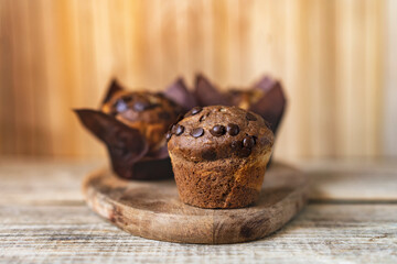 Soft and moist chocolate banana muffins with dark chocolate drops in wooden box, rustic table. Homemade baked twisted cupcakes. Natural light, selective focus, copy space