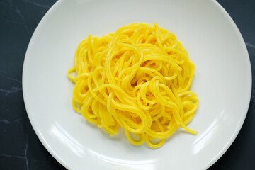 The noodles are in a round white plate placed on table.yellow noodle.top view food.