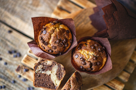 Soft and moist chocolate banana muffins with dark chocolate drops in wooden box, rustic table. Homemade baked twisted cupcakes. Natural light, selective focus, copy space