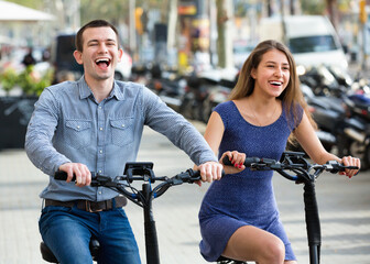 Obraz premium Charming smiling man and woman with electrkc bikes in vacation on city street