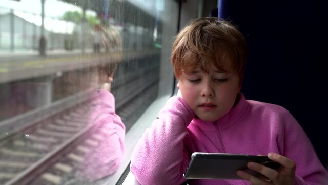 child with smartphone in suburban train, playing games, surfing internet and boring