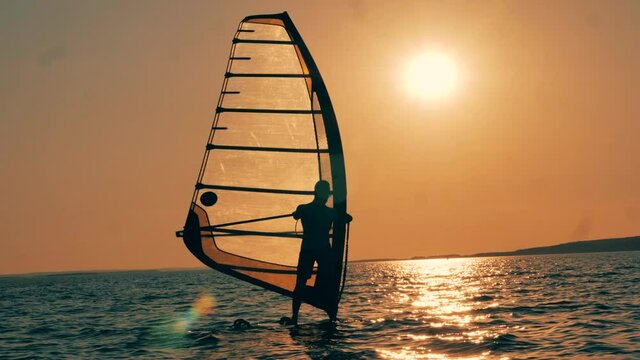 A man is crossing sunset waters on a windsurf board