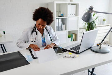 Woman doctor with stethoscope looking at medical papers at her office working hard