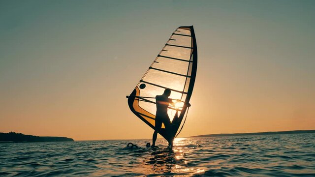 A man is sailboarding in the ocean at sunset
