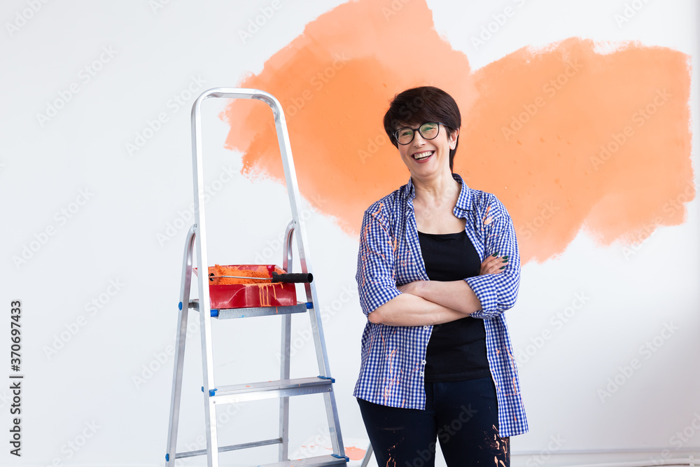 Wall mural Repair in the apartment. Happy middle-aged woman paints the wall with paint.