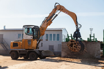 An industrial loader loads logs into a conveyor at a sawmill