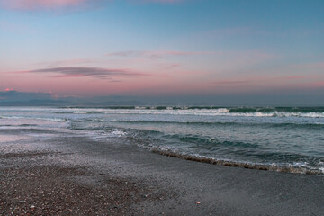 Sea with waves, sea foam and sandy beach at dusk