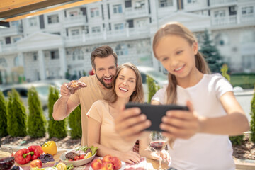 Fair-haired girl in white tshirt making selfie with happy parents