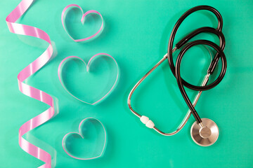 Stethoscope with heart ribbon on green paper background.