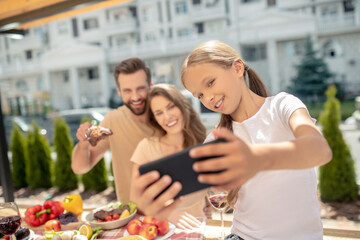 Fair-haired girl in white tshirt making selfie with parents
