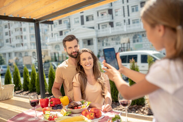 Fair-haired girl making picture of her smiling parents