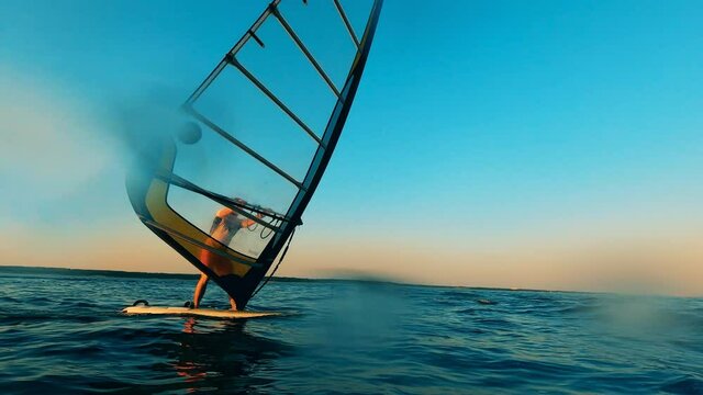 Sunset sea and a windsurfer managing a sailboard