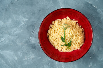 Healthy and dietary side dish - couscous porridge in a burgundy bowl on a concrete background. Top...