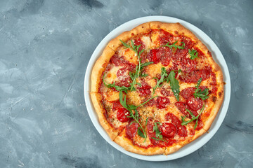 Italian pizza with salami, arugula and parmesan on a white plate. Concrete background. Top view. Copy space