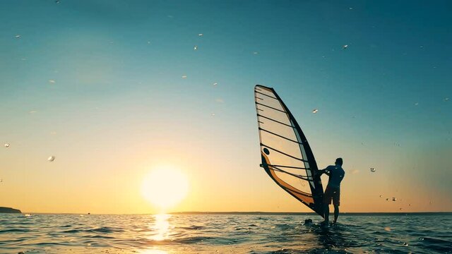 A man is sailboarding along the shore at sunset