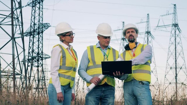 Energy workers are planning a project near electrical towers. Enenrgy engineers inspecting a power line.