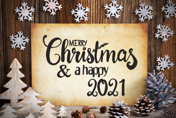 Obraz na płótnie Canvas Old Paper With English Text Merry Christmas And Happy 2021. Christmas Decoration Like Tree, Fir Cone And Snowflakes. Brown Wooden Background