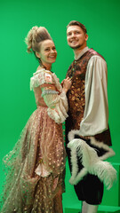 Fototapeta premium On Big Film Studio Two Talented Actors of Female and Male Playing a Beautiful Lovely Couple Wearing Renaissance Clothes and Smiling on Camera. The Scene on Green Screen.