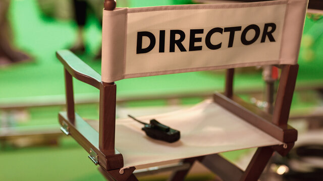 On Film Studio Set Close Up Shot Of Empty Director's Chair. In The Background Professional Crew Shooting Green Screen Scene With Actors For History Movie.