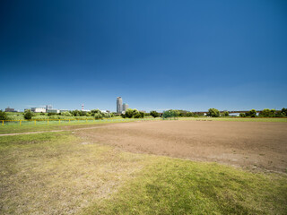 Fototapeta premium Boisko baseballowe na niebieskim niebie i korycie rzeki w sierpniu. Pejzaż miasta z tyłu to Kawaguchi City w prefekturze Saitama.