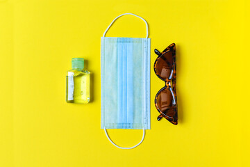 Protective mask,  sunglasses and sanitizer on yellow background. trendy accessory. minimalism fashion concept 2020. Top view travel or vacation concept, summer traveler accessories