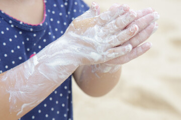 Close up image of child's hands applying sunscreen protection cream on the beach. Sun blocking lotion for protecting baby from sun during summer vacation. Children health care and skin care during tra