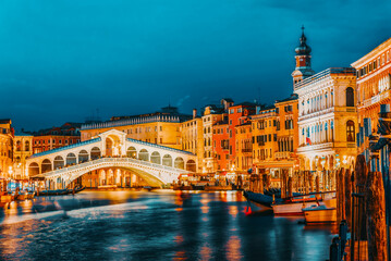 Rialto Bridge (Ponte di Rialto) or Bridge of Sighs and view of the most beautiful canal of Venice - Grand Canal and boats, gondolas, mansions along. Night view. Italy.