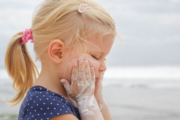 Cute little toddler girl applying sunscreen protection cream on the beach. Sun blocking lotion for protecting baby from sun during summer vacation. Children skin care during travel time.