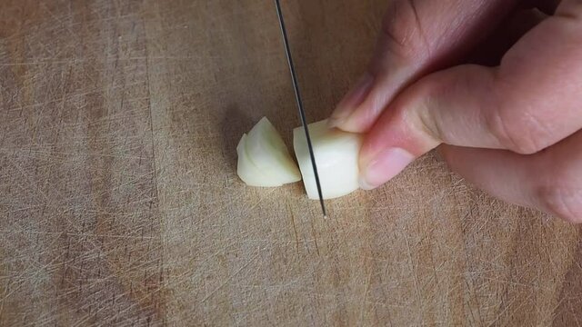 A clove of garlic is cut by a cook on a wooden cutting Board.