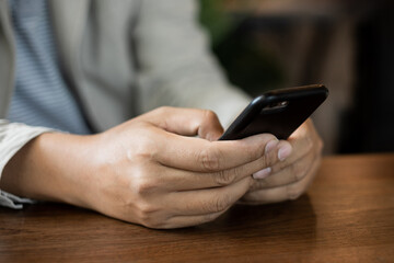 Close up of businessman's hands holding and typing on black cellphone for business communication in the cafe with a cup of coffe on wooden table. Business stock photo.
