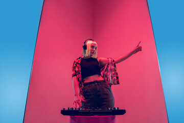 Drive. Young female musician in headphones performing on blue-red background in neon light. Concept...