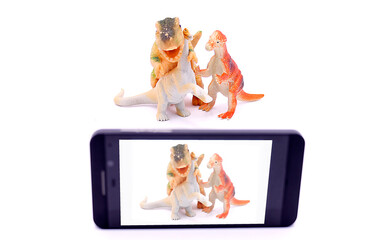 Dinosaur toys are photographed on a smartphone on a white background.