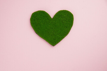 Earth day, ecology concept and environmental preservation. Green heart from grass on pink background. Love nature and save the planet and world.